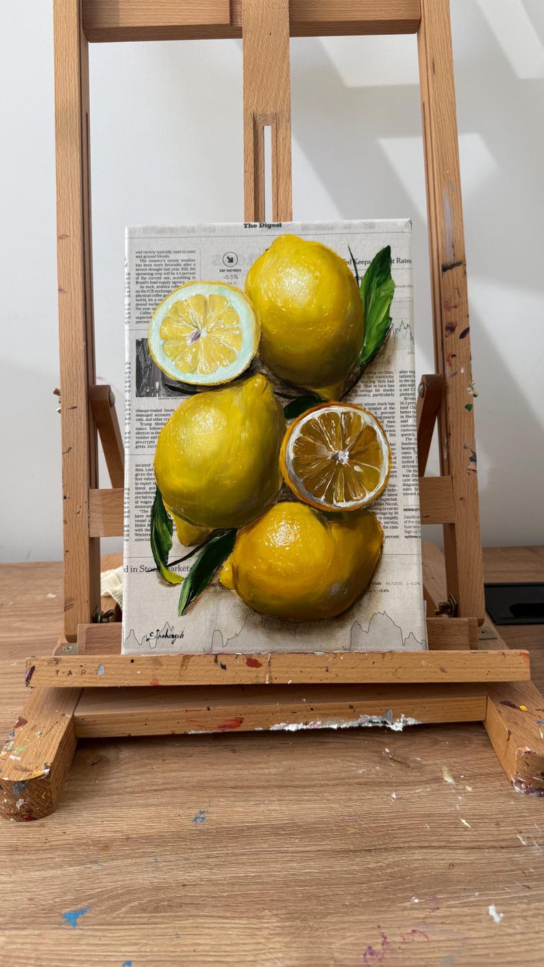 May include: A rectangular canvas painting featuring four bright yellow lemons, two of which are sliced in half, with green leaves. The lemons are painted over a background of printed newspaper text titled The Digest, with a signature at the bottom.