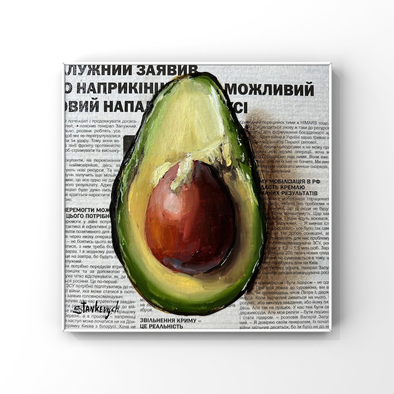 May include: A painting of a halved avocado with a green exterior and a brown pit. The avocado is painted on top of a newspaper article with the text "ЛУЖНИИ ЗАЯВИВ О НАПРИКІНИ ВИЙ НАПАД" and "ЗВІЛЬНЕННЯ КРИМУ - ЦЕ РЕАЛЬНІСТЬ."