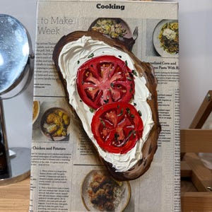 May include: A painting of a slice of bread topped with white cream cheese and two red tomato slices. The painting is on a canvas with a newspaper background. The newspaper text includes the words "Cooking", "to Make", "Week", "Chicken and Potatoes", and "melized Corn and zus Pasta With Ri".
