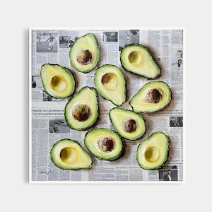 May include: A painting of a still life featuring a dozen avocados arranged on a newspaper background. The avocados are cut in half, revealing their green flesh and brown seeds. The newspaper is printed in black and white and features text in Russian.