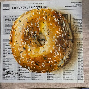 May include: A painting of a bagel with sesame seeds on a newspaper background. The newspaper headline reads "ВІВТОРОК, 21 ВЕРЕСНЯ".