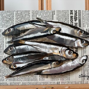 May include: A painting of a group of silver fish on a newspaper background. The fish are arranged in a pile, with their tails pointing towards the top of the image. The newspaper is printed in Russian and has the words "СИЛА-ВІРИ" and "подь Зи" visible. The painting is signed "STANKEYUCH" in the lower right corner.