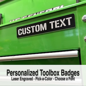 May include: A black metal toolbox badge with the text "CUSTOM TEXT" engraved in silver. The badge is attached to a green toolbox.