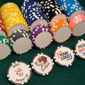 May include: Stacks of colorful poker chips in red, yellow, blue, black, orange, pink, and green. Some chips have custom designs, including a dog illustration, a logo, and text that reads "DIEGO'S BIRTHDAY TRIP" and "DIEGO'S BIRTHDAY PARTY".