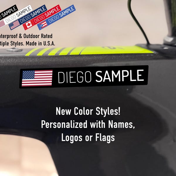 Puede incluir: Una calcomanía rectangular con la bandera de los Estados Unidos y el texto DIEGO SAMPLE en letras mayúsculas blancas sobre un fondo negro, aplicada al marco oscuro de una bicicleta con rayas amarillas y texto adicional.