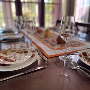 Peut inclure: Une table &agrave; manger dress&eacute;e pour un repas, avec des assiettes blanches au design automnal, des couverts et des verres &agrave; vin. Un chemin de table d&eacute;coratif avec une bordure orange et des motifs d'automne.
