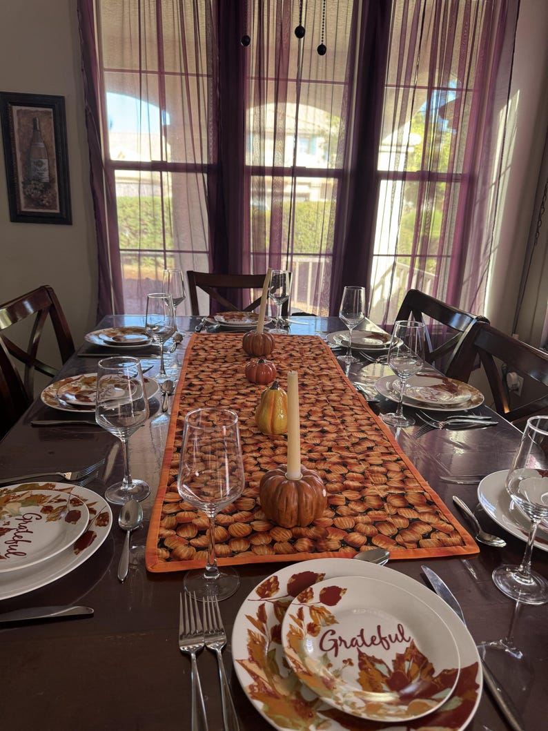 Peut inclure: Une table de salle &agrave; manger dress&eacute;e pour un repas, avec des assiettes portant le mot "Grateful" et des motifs de feuilles d'automne. Un chemin de table sur le th&egrave;me de la citrouille, des citrouilles d&eacute;coratives et des bougies sont pr&eacute;sents.