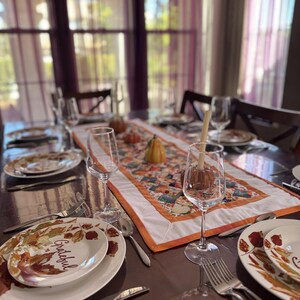 Peut inclure: Une table &agrave; manger dress&eacute;e pour un repas d'automne. Les assiettes blanches pr&eacute;sentent un motif de feuilles et le mot "Grateful". Un chemin de table color&eacute; avec des citrouilles et des courges est au centre. Verres &agrave; vin et couverts compl&egrave;tent le d&eacute;cor.
