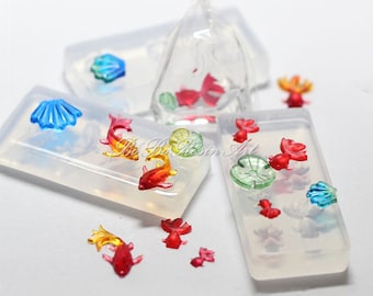 May include: A set of clear silicone molds for resin casting, featuring a variety of shapes including fish, seashells, and lily pads. The molds are shown with colorful resin castings inside.