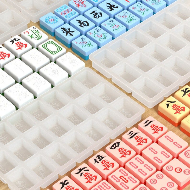 May include: A set of white, blue and pink mahjong tiles with Chinese characters and symbols. The tiles are arranged in a grid pattern on a white surface. There are also several empty tile holders.