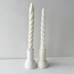 May include: Two white twisted candles in white ceramic holders. The candles are different sizes.