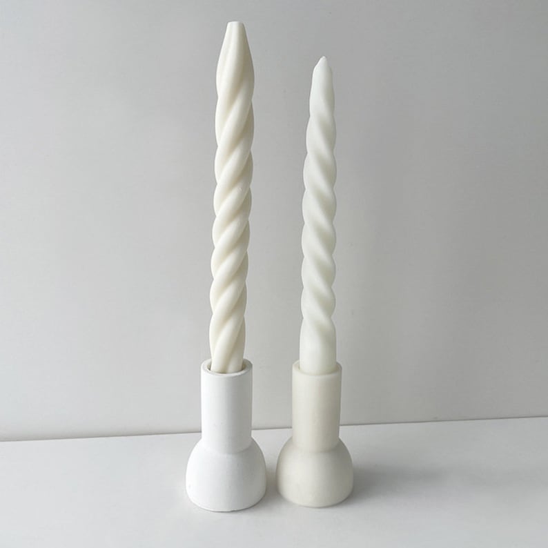 May include: Two white twisted candles in white ceramic holders. The candles are different sizes.