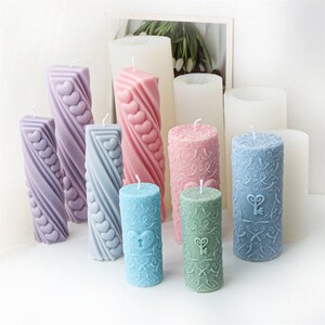 May include: Assortment of decorative pillar candles in various colours and designs. The candles feature heart, keyhole, and floral patterns.