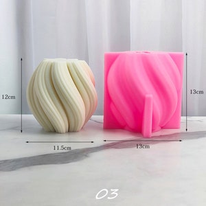 May include: Two silicone candle molds, one white and one pink. The white mold is round and has a swirl design. The pink mold is square and has a swirl design. The molds are 12 cm tall and 11.5 cm wide. The pink mold is 13 cm wide. The molds are on a white marble surface. 03