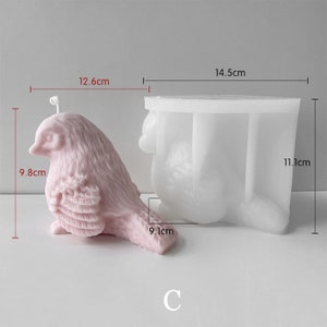 May include: A pink bird-shaped candle and a white silicone mold. The candle is 9.8 cm tall, 12.6 cm long, and 9.1 cm wide. The mold is 11.1 cm tall and 14.5 cm wide. The letter "C" is at the bottom.