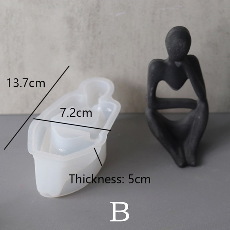 Może przedstawiać: Biała silikonowa forma w kształcie siedzącej osoby. Forma ma 13,7 cm długości, 7,2 cm szerokości i 5 cm grubości. Litera "B" jest nadrukowana pod formą.