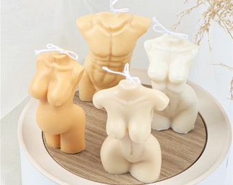 May include: Four nude-colored candles shaped like human torsos. The candles are arranged on a wooden tray with a white base.