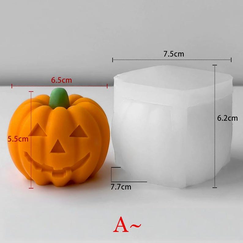 K&ouml;nnte beinhalten: Eine orangefarbene K&uuml;rbisform mit einem geschnitzten Gesicht, 6,5 cm breit und 5,5 cm hoch. Daneben eine wei&szlig;e, quadratische Form, 7,7 cm breit und 6,2 cm hoch. Der K&uuml;rbis hat einen gr&uuml;nen Stiel. Der Text "A~" steht unten.