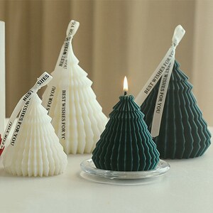 以下が含まれることがあります： 白い、緑色の、濃い緑色の3つのクリスマスツリーの形をしたキャンドル。それぞれのキャンドルには、「あなたへの最高の願い」というテキストが書かれたリボンが結ばれています。