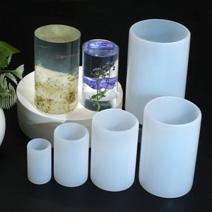 Peut inclure: Ensemble de sept moules en silicone cylindriques transparents et blancs pour la coulée de résine. Les moules sont de tailles différentes et sont disposés sur une surface blanche.