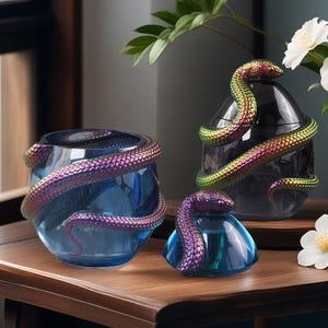Puede incluir: Tres recipientes de vidrio iridiscente con asas en forma de serpiente. Los recipientes son azules, verde azulado y negros. Las serpientes son una mezcla de verde y morado.