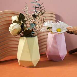 May include: Two geometric vases, one yellow and one pink, with a floral arrangement of white roses and daisies.