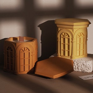 May include: Two yellow hexagonal candle holders with a decorative arch design. The candle holders are made of a smooth, matt material and have a slightly textured surface. The candle holders are empty and ready to be filled with candles.