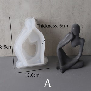 Może przedstawiać: Biała silikonowa forma do tworzenia betonowej rzeźby osoby siedzącej z podbr&oacute;dkiem na dłoni. Forma ma 8,8 cm wysokości, 13,6 cm szerokości i 5 cm grubości. Gotowa rzeźba jest pokazana obok formy.