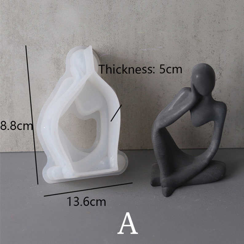 Może przedstawiać: Biała silikonowa forma do tworzenia betonowej rzeźby osoby siedzącej z podbr&oacute;dkiem na dłoni. Forma ma 8,8 cm wysokości, 13,6 cm szerokości i 5 cm grubości. Gotowa rzeźba jest pokazana obok formy.