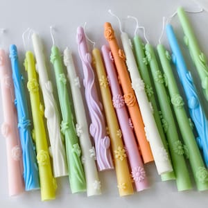 May include: Assortment of colourful taper candles with floral and snowflake designs. The candles are approximately 10 inches long and are made of a smooth, wax material.