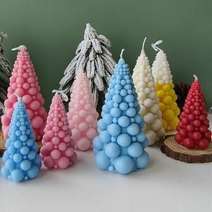 Könnte beinhalten: Sortiment an bunten Weihnachtsbaumkerzen. Die Kerzen sind aus Wachs und haben eine strukturierte, blasenartige Oberfläche. Die Kerzen sind in verschiedenen Farben, darunter blau, rosa, rot, weiß und gelb.