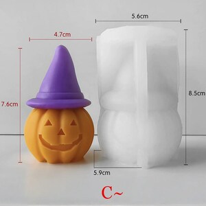 K&ouml;nnte beinhalten: Ein Set aus Kerze und Form zum Thema Halloween. Die orangefarbene K&uuml;rbiskerze, 7,6 cm hoch und 4,7 cm breit, hat ein geschnitztes Gesicht und einen lila Hexenhut. Die wei&szlig;e Form, 8,5 cm hoch und 5,6 cm breit, dient zur Herstellung &auml;hnlicher K&uuml;rbisse. Text "C~" unten.