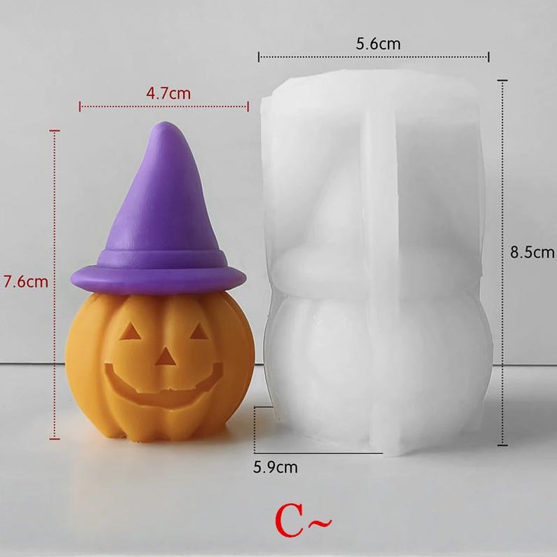 K&ouml;nnte beinhalten: Ein Set aus Kerze und Form zum Thema Halloween. Die orangefarbene K&uuml;rbiskerze, 7,6 cm hoch und 4,7 cm breit, hat ein geschnitztes Gesicht und einen lila Hexenhut. Die wei&szlig;e Form, 8,5 cm hoch und 5,6 cm breit, dient zur Herstellung &auml;hnlicher K&uuml;rbisse. Text "C~" unten.