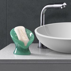 May include: A green soap dish with a white bar of soap that says "pro-bakes" on it. The soap dish is sitting on a white countertop next to a white sink.