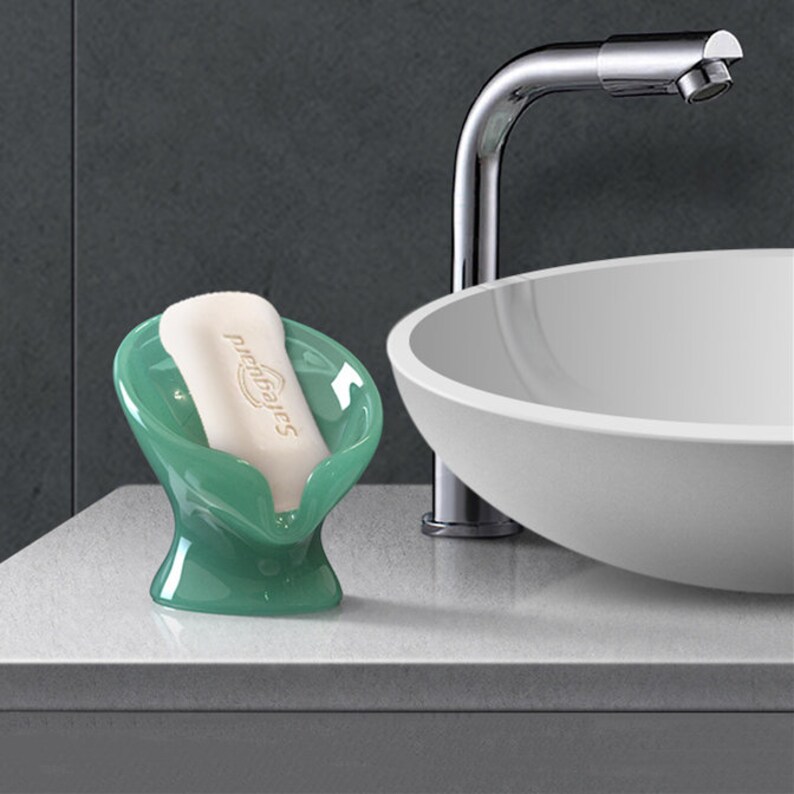 May include: A green soap dish with a white bar of soap that says "pro-bakes" on it. The soap dish is sitting on a white countertop next to a white sink.
