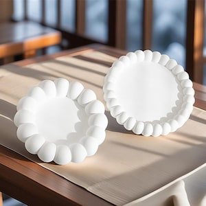 May include: Two white ceramic plates with a raised, textured rim. The plates are round and have a smooth, white interior.