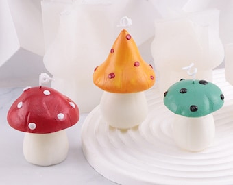 May include: Three mushroom-shaped candles, one red with white dots, one orange with red dots, and one green with black dots. The candles are on a white circular base.