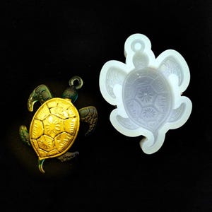 May include: A gold-coloured turtle pendant with a detailed shell design, and a white silicone mould of the same turtle pendant.