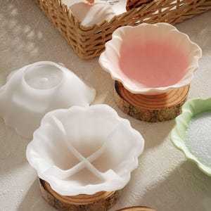 May include: Three white ceramic bowls with scalloped edges. The bowls are on wooden bases. One bowl has four sections, one is plain, and one is pink.