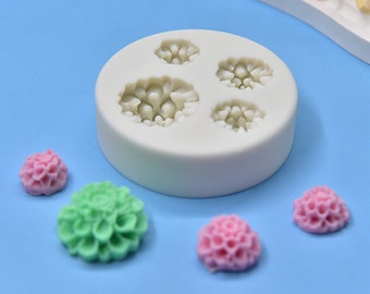 May include: White silicone mold with four flower-shaped cavities. Four small, colorful, flower-shaped decorations are shown next to the mold.