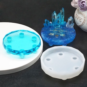 May include: Two clear blue resin molds with six indentations on the bottom. The molds are on a white surface. One mold is filled with a blue resin crystal cluster.