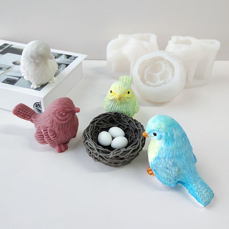 May include: A selection of bird-themed ornaments and crafting supplies. Features a white bird figurine, a maroon bird, a green and yellow bird, a blue bird, a nest with three eggs, and white silicone moulds.