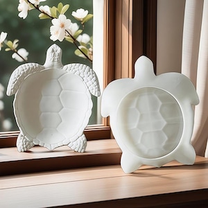 Pode incluir: Dois pratos de cerâmica branca em forma de tartaruga. Os pratos são lisos e têm um desenho em relevo de carapaça de tartaruga.
