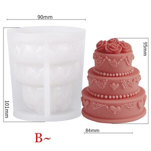 Puede incluir: Un molde de silicona para pastel de boda de tres niveles con un di&aacute;metro de 90 mm, una altura de 101 mm y una base de 84 mm. El molde est&aacute; hecho de silicona blanca y tiene un dise&ntilde;o detallado de flores y corazones. El molde se muestra junto a un pastel de boda rosa con acentos blancos.