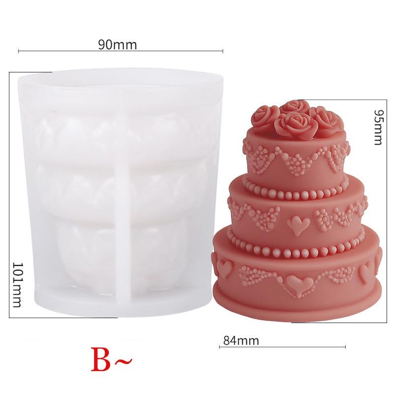 Puede incluir: Un molde de silicona para pastel de boda de tres niveles con un di&aacute;metro de 90 mm, una altura de 101 mm y una base de 84 mm. El molde est&aacute; hecho de silicona blanca y tiene un dise&ntilde;o detallado de flores y corazones. El molde se muestra junto a un pastel de boda rosa con acentos blancos.