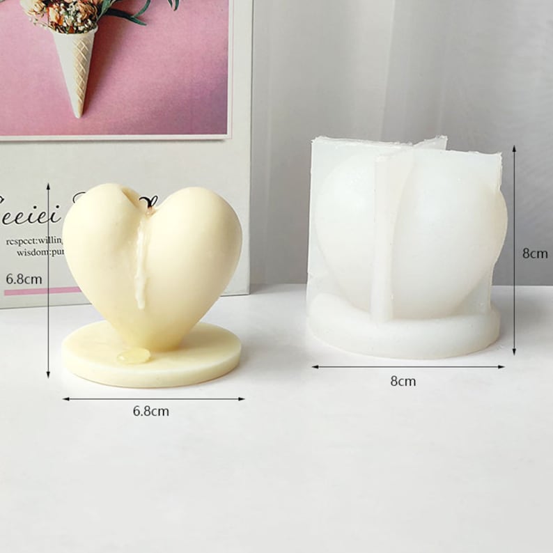Op de afbeelding: Een witte hartvormige kaars met een druppelend wasontwerp. De kaars is 6,8 cm hoog en 6,8 cm breed. Een witte siliconen mal voor het maken van hartvormige kaarsen is ook afgebeeld. De mal is 8 cm hoog en 8 cm breed.
