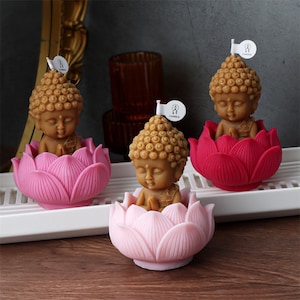 May include: Three small Buddha candles, each sitting in a lotus flower. The candles are brown and the lotus flowers are pink and red.