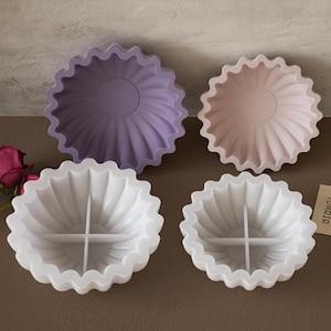 May include: Four silicone cake moulds in different colours. Two moulds are white with a divided centre, and two moulds are single-cavity, one purple and one pink.