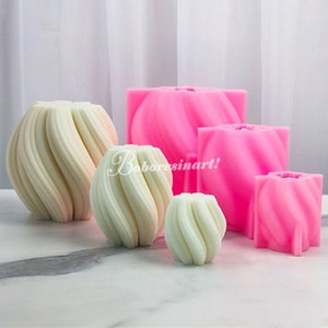 May include: Four pink silicone moulds for making candles. The moulds are shaped like a swirl and are different sizes. The moulds are on a white surface.