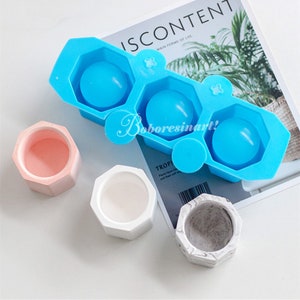 May include: A blue silicone mould with three hexagonal cavities for making small planters. Three finished planters are shown: one pink, one white, and one grey with a marbled pattern.